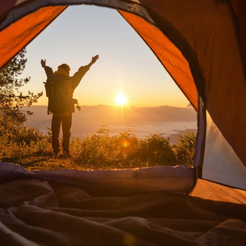 Hiker stand at the camping front orange tent and backpack in the mountains. Backpacker looking into the distance